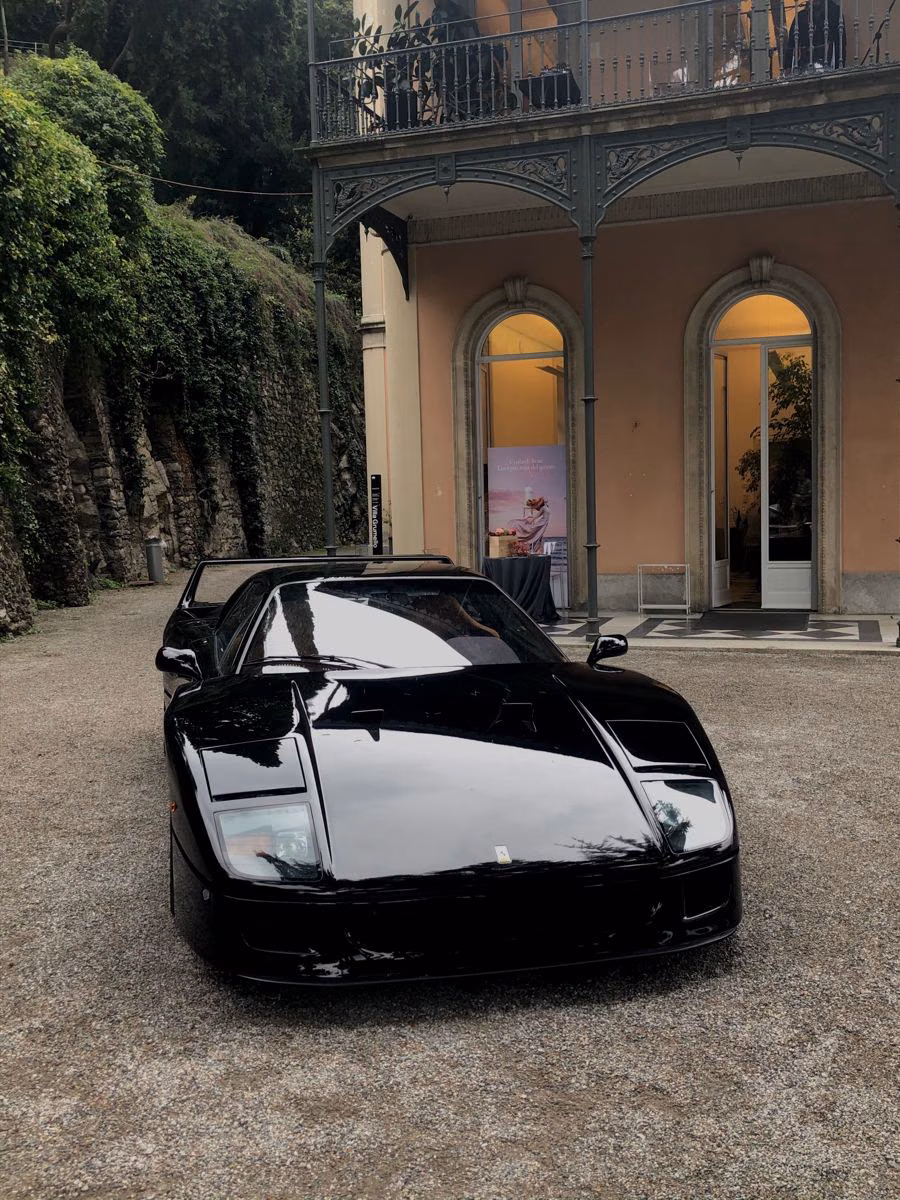 A low black sports car with a wedge-shaped nose parked before a classical entrance.