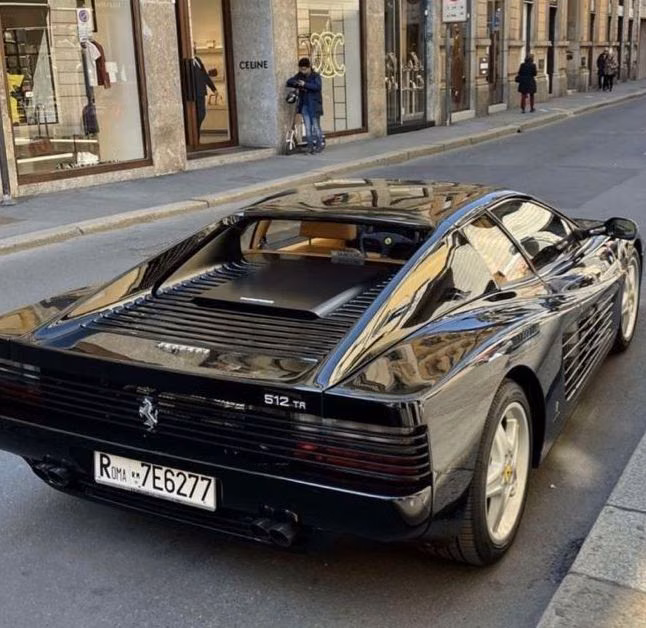 A black Ferrari 512 TR viewed from behind on a European city street.