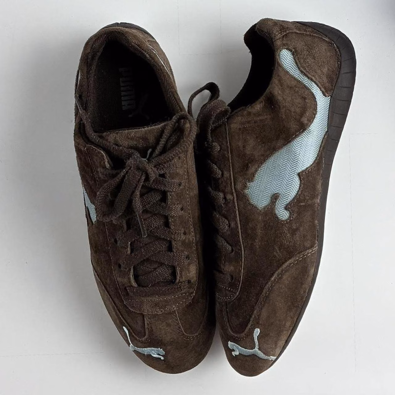 A pair of brown suede trainers with a turquoise Puma formstrip photographed from above.