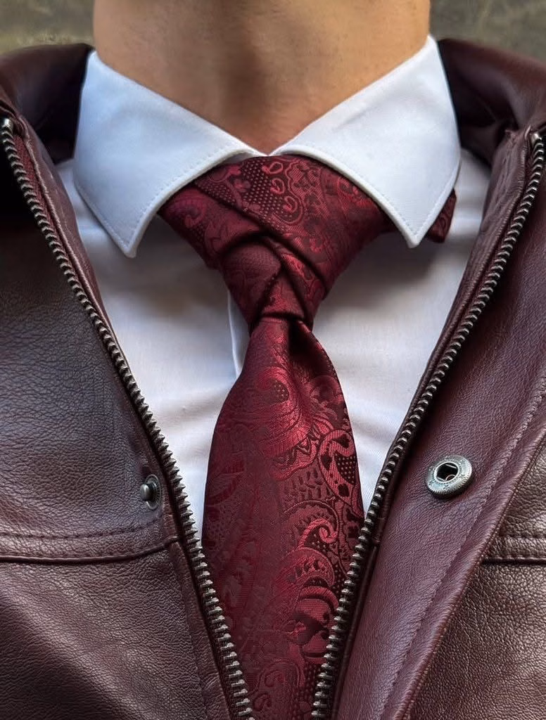 A close crop of a white shirt, burgundy paisley tie and burgundy leather jacket.