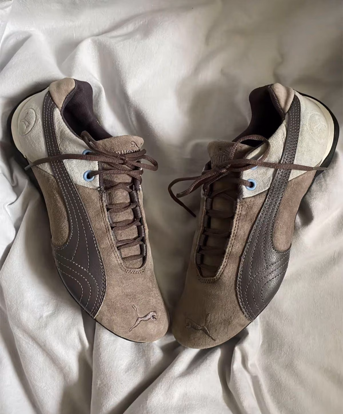 A pair of brown Puma trainers with light panels resting on pale bedding.