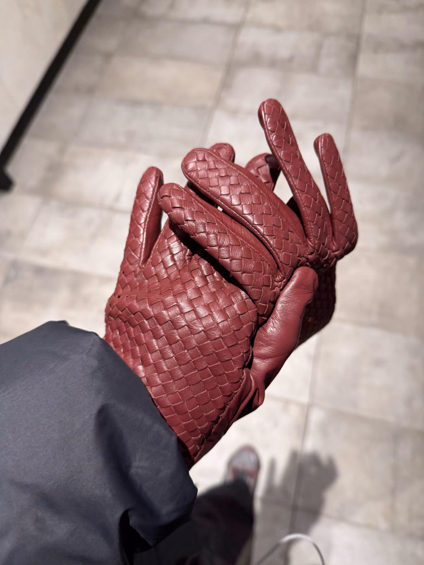 A pair of burgundy woven-leather gloves held up during a walk.