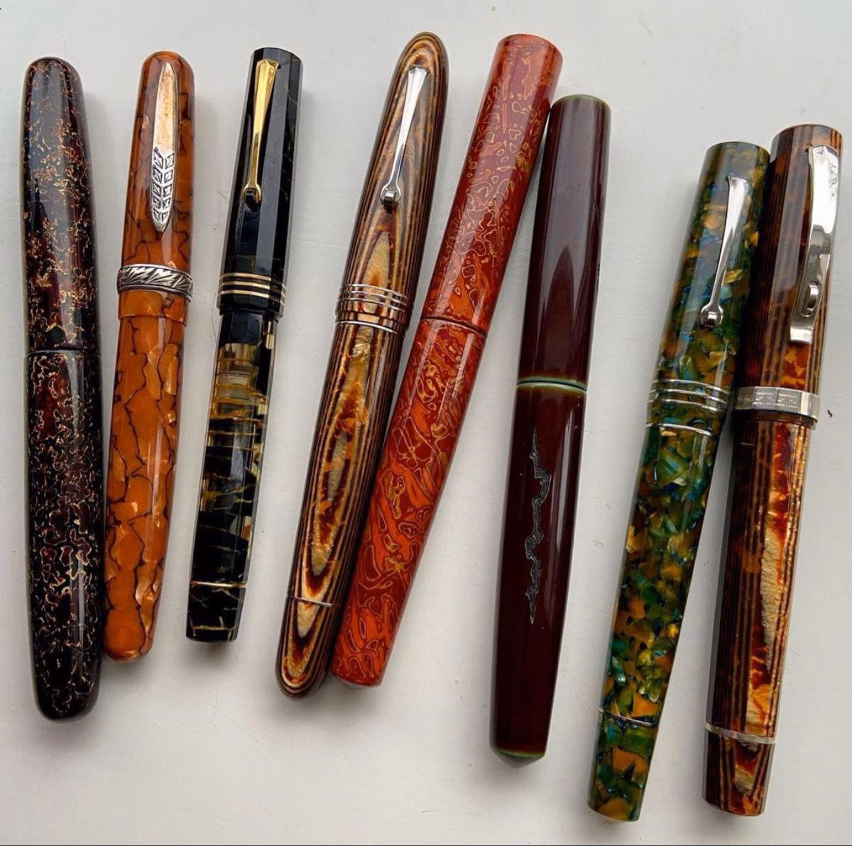 Five different fountain pens arranged in a row on a white surface.