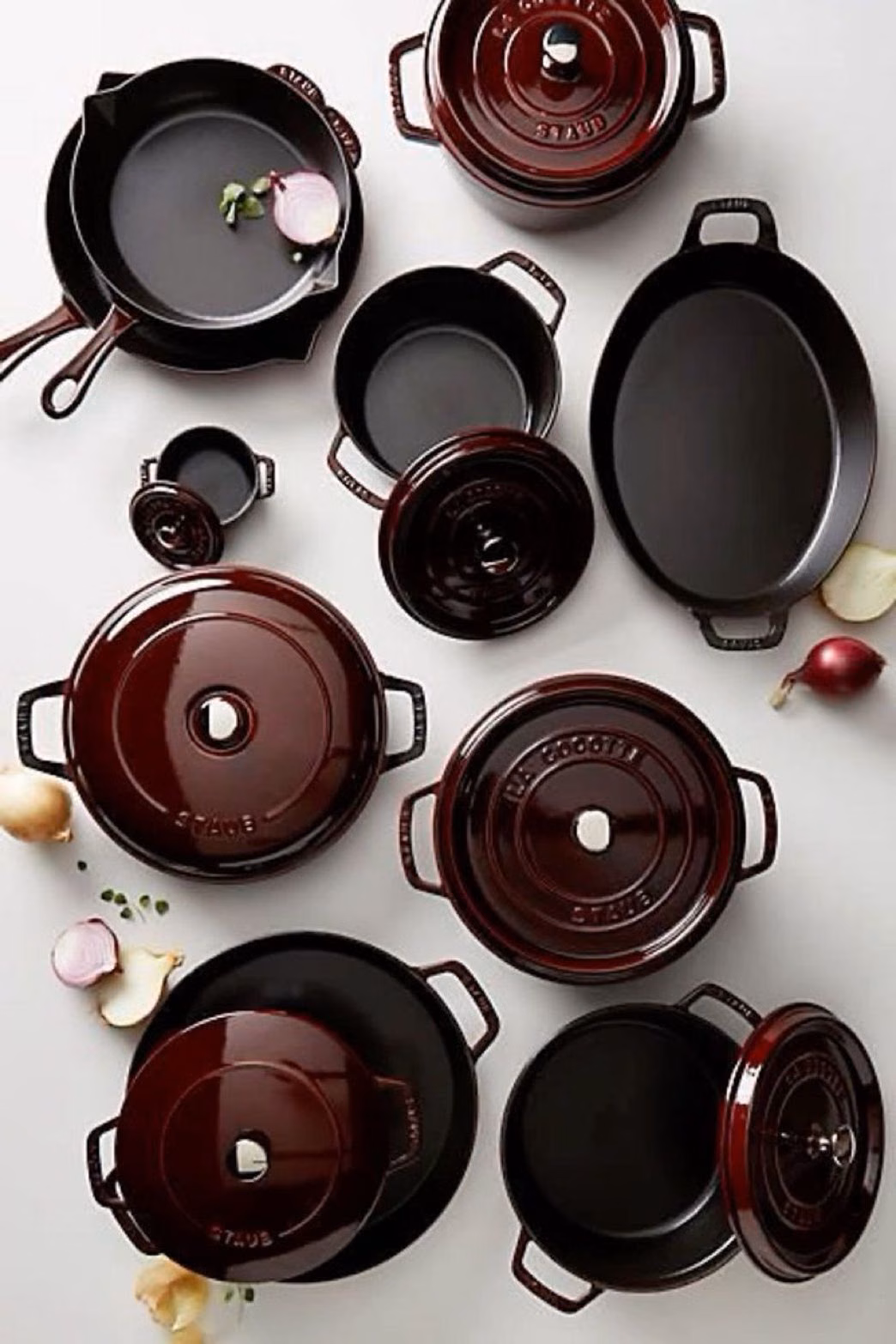 Pots and pans arranged on a white table with onions placed around them.