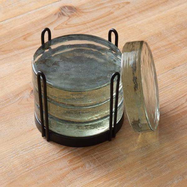 An empty glass on a wooden table beside a metal holder.