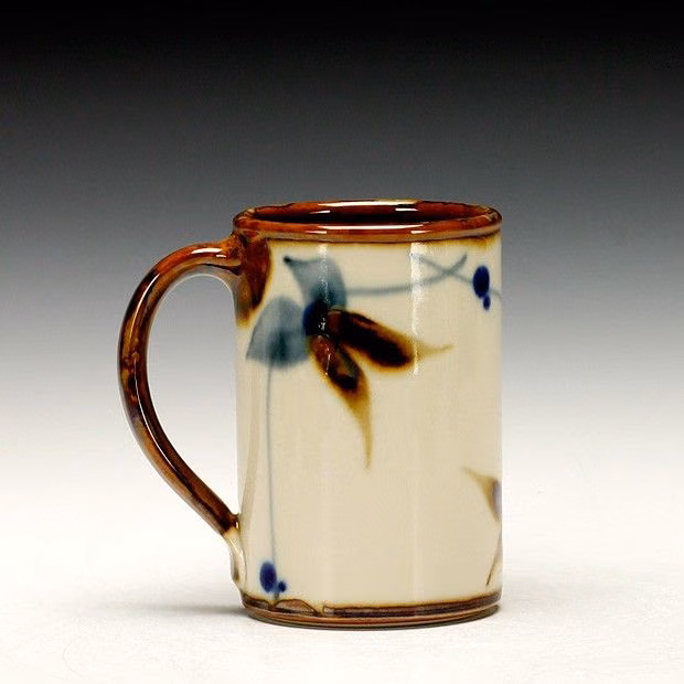 A white and brown coffee cup with blue flowers inside, set against a grey background.