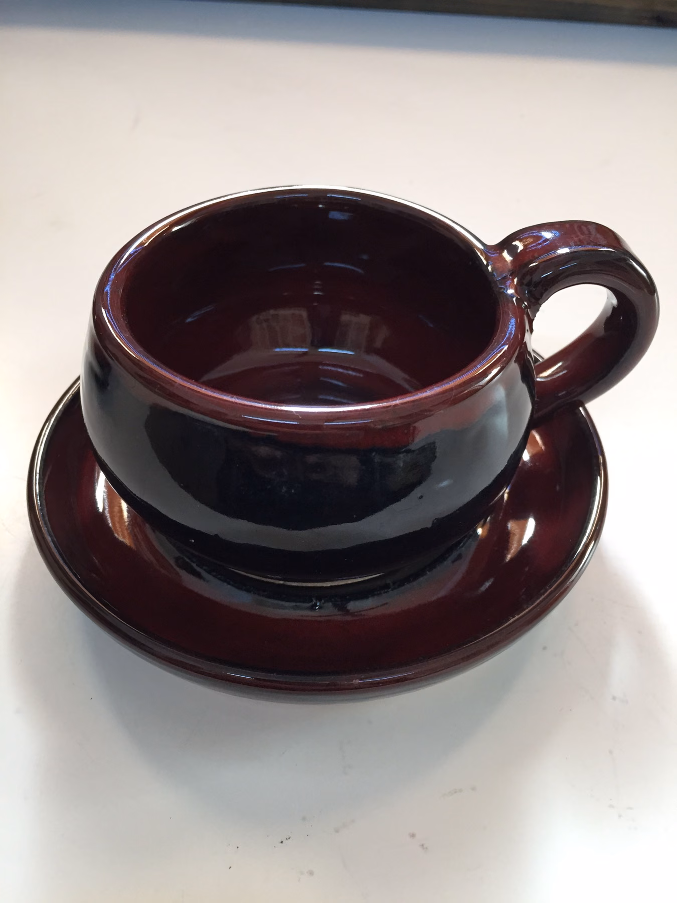 A red cup and saucer on a white worktop beside a black plate.