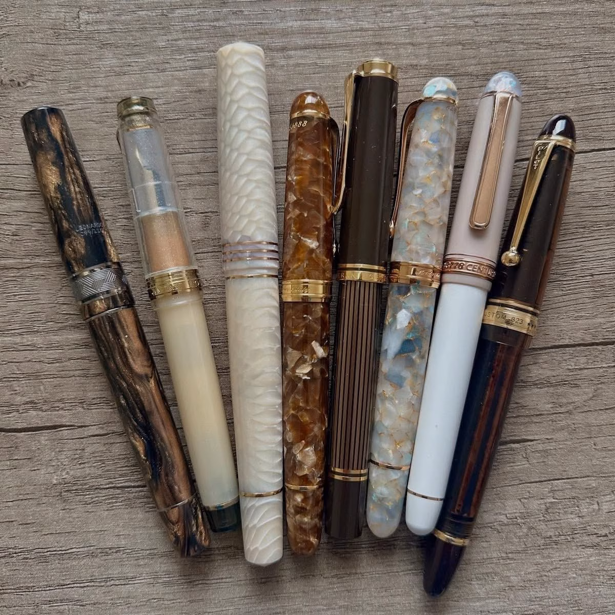 Different pens arranged in a row on a wooden surface.