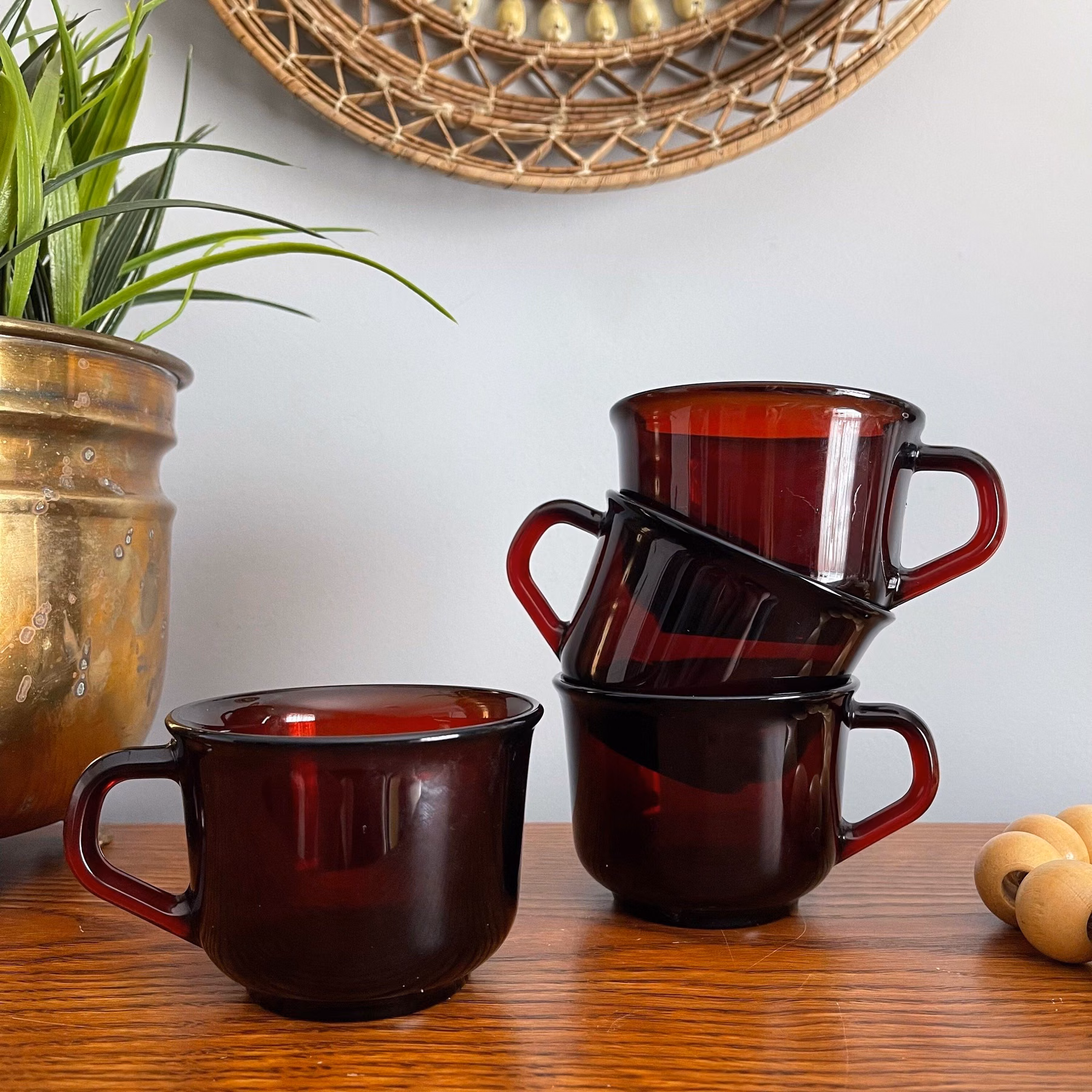 Three coffee cups on a wooden table beside a potted plant.