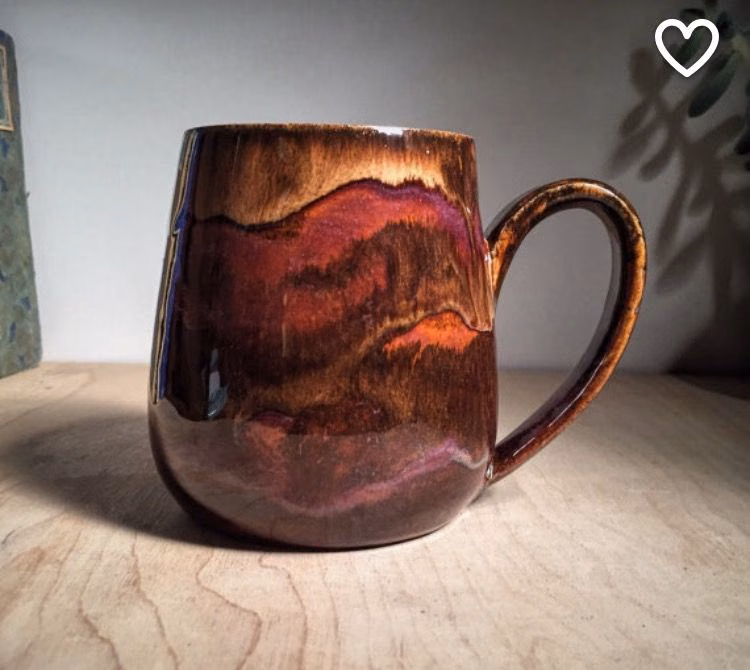 A coffee cup on a wooden table beside a potted plant.