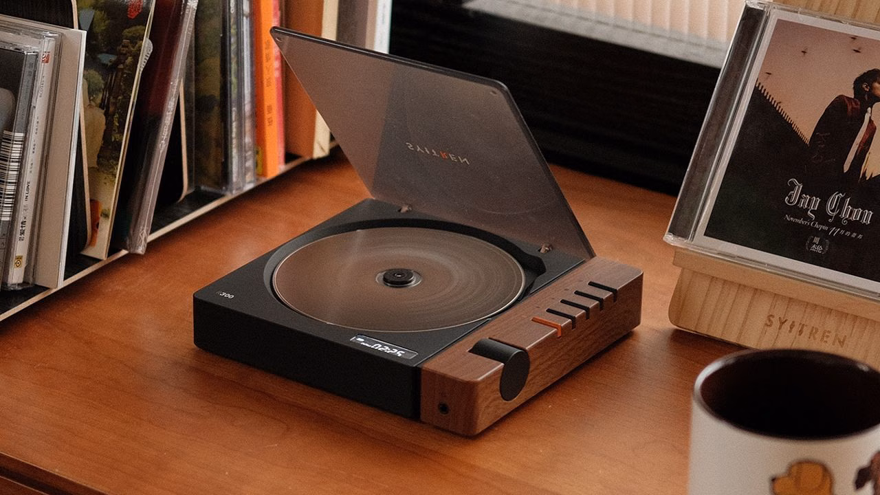 A record player on a wooden table beside a coffee cup and a vinyl record.