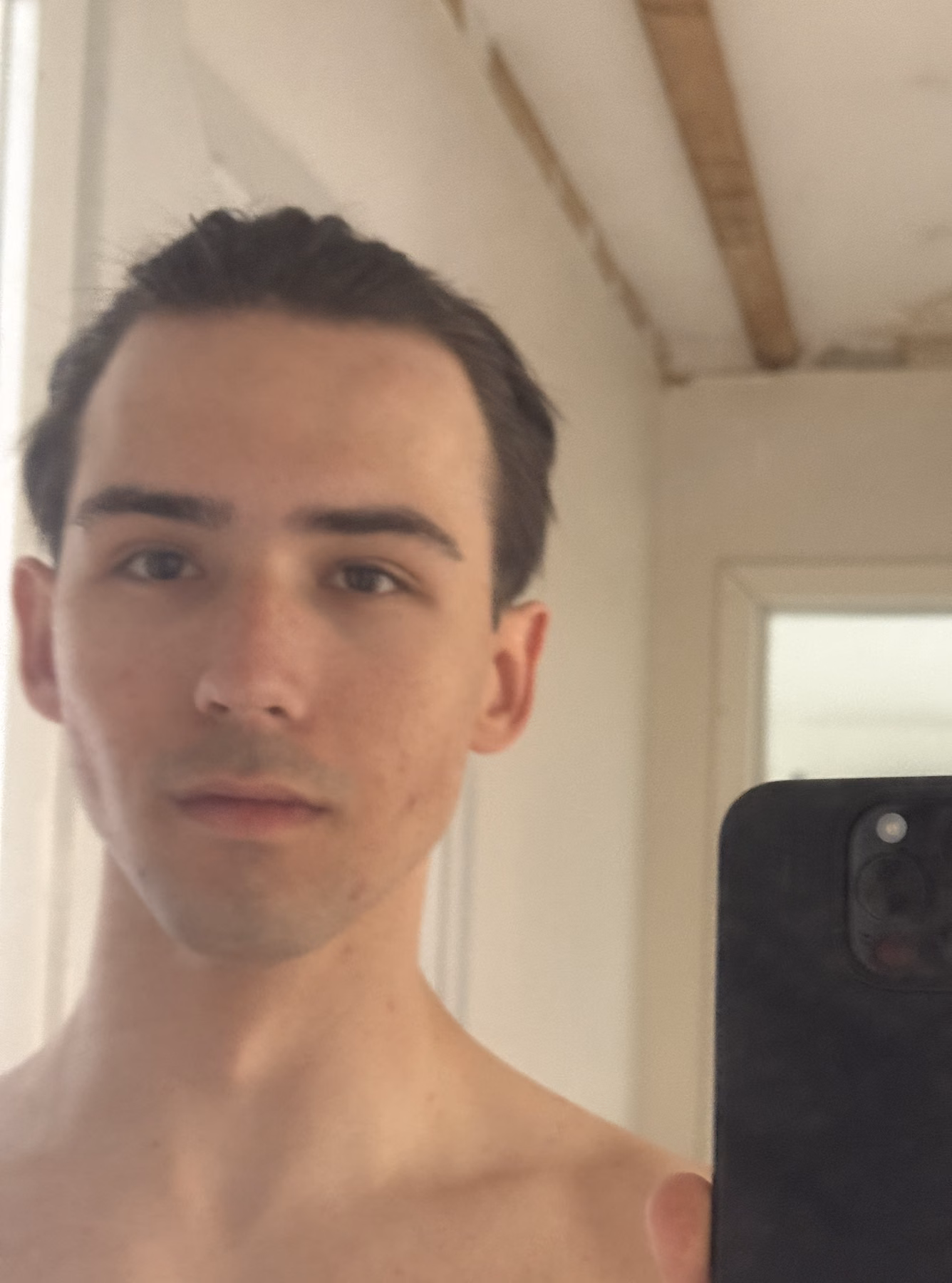 A close mirror portrait of Malthe with his hair tied back in a bright room.
