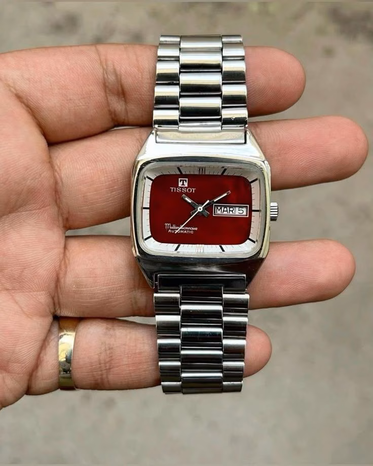 A rectangular steel Tudor watch with a burgundy dial held in one hand.