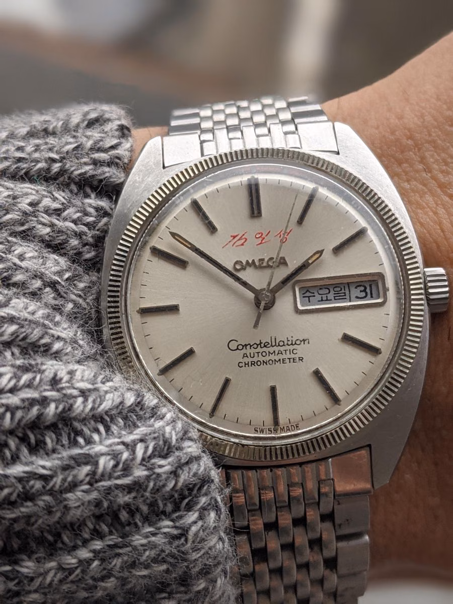 A vintage steel Omega Constellation with a light dial worn over a grey knit cuff.